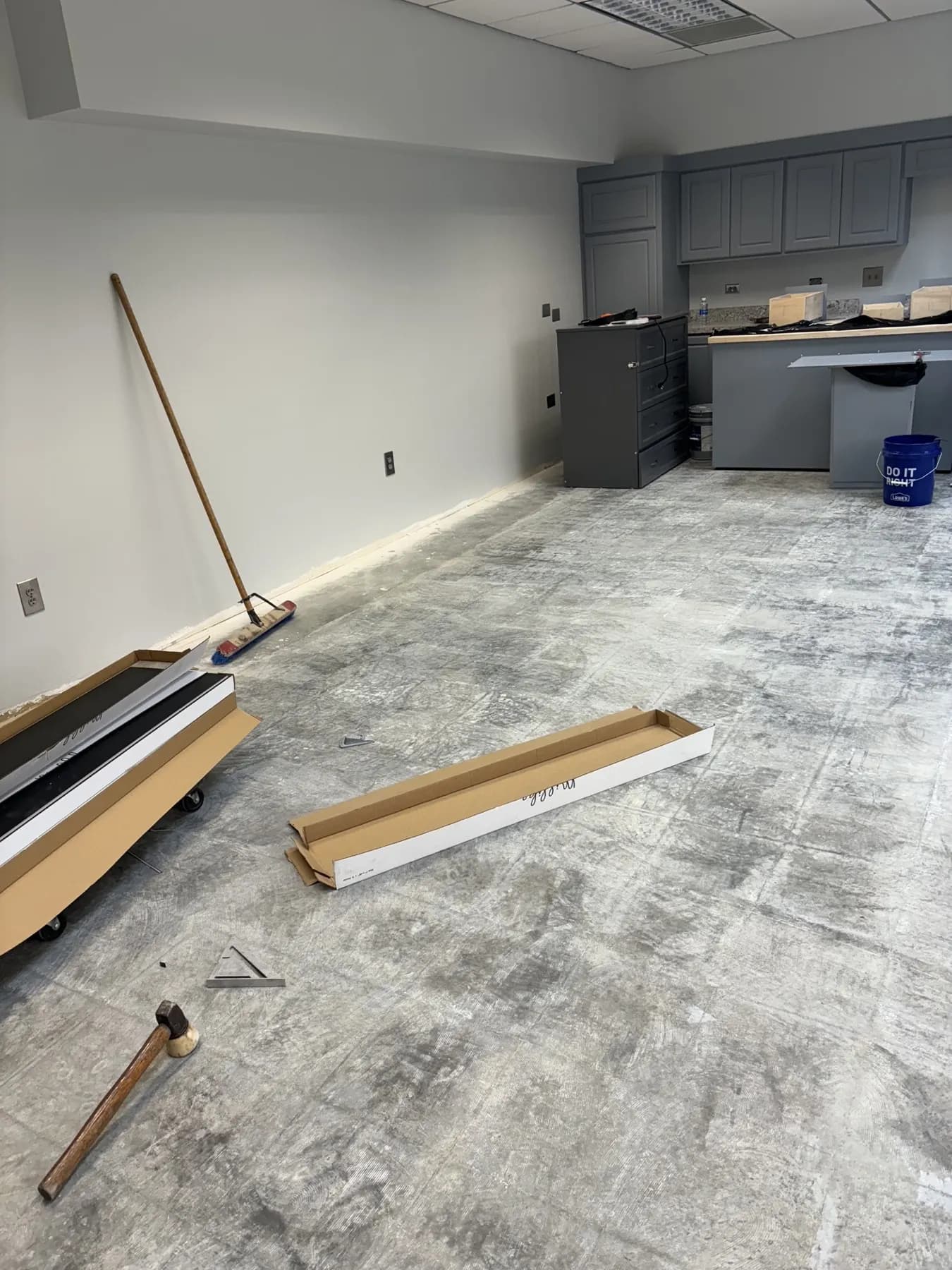 Office break room with new gray cabinets over a bare, scraped concrete floor