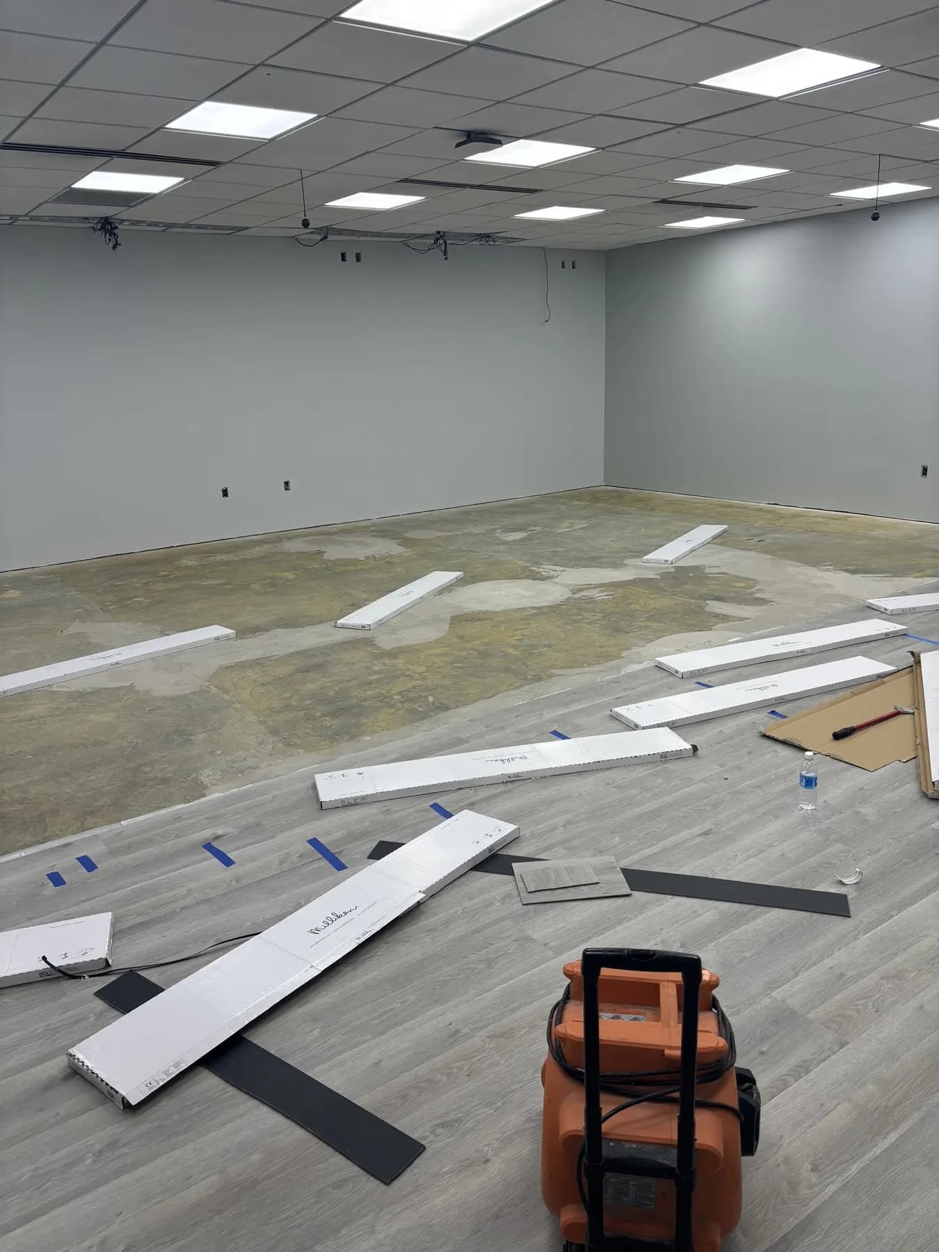 In progress: gray vinyl plank being laid across a patched concrete slab in a large open room